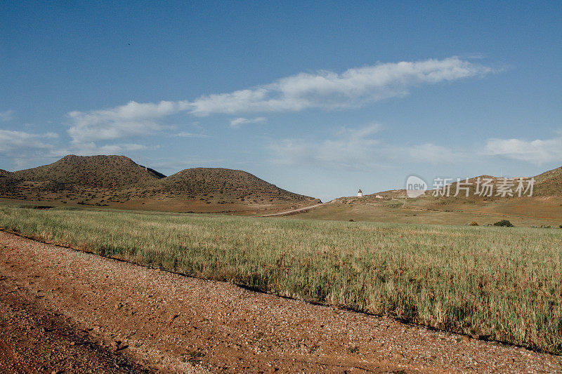 在西班牙阿尔梅里亚的一个小镇“Cabo de Gata”，在远处的干燥的草地和山丘上看到的一条干旱的道路。